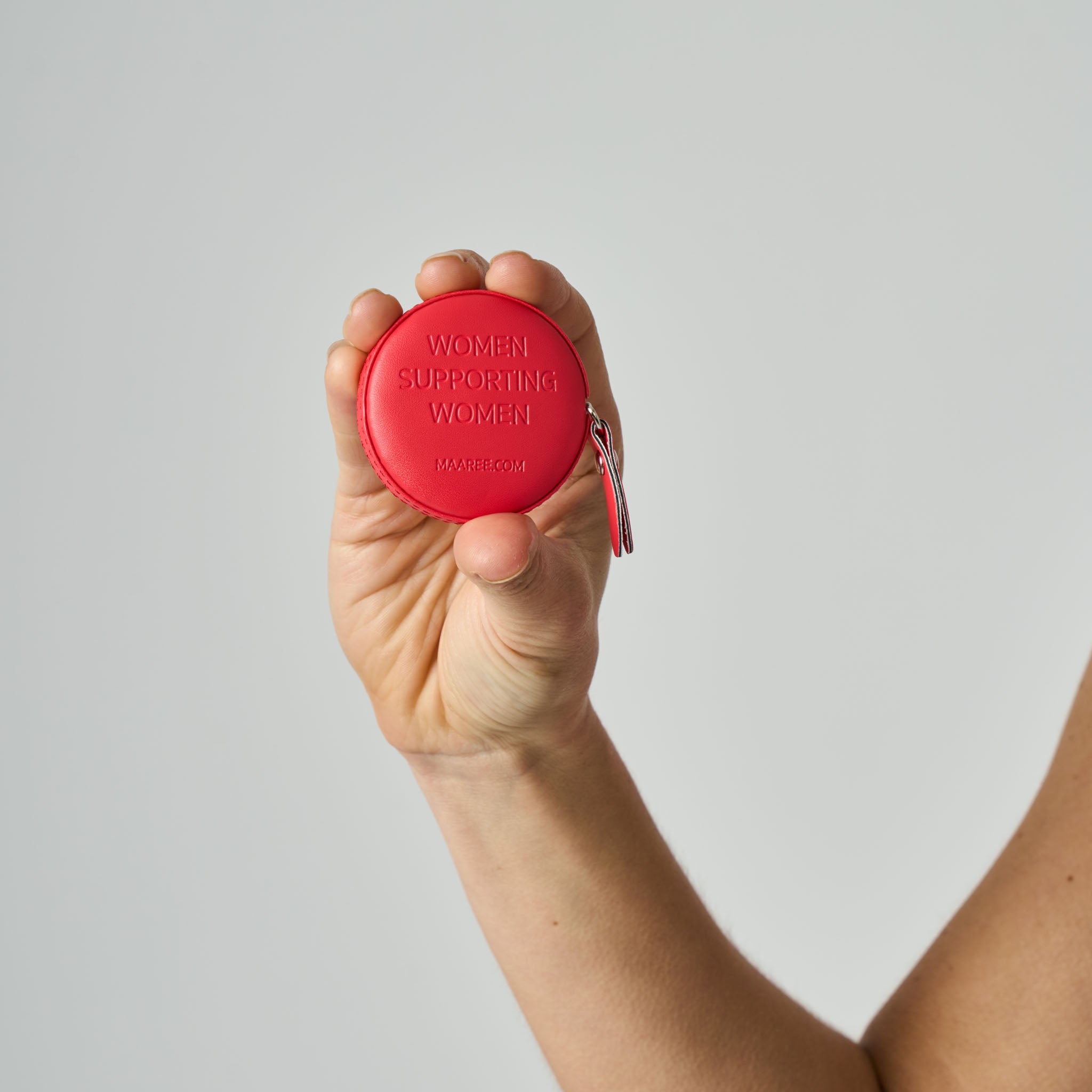 Hand holding a red tape measure with 'Women Supporting Women' text on a light grey background