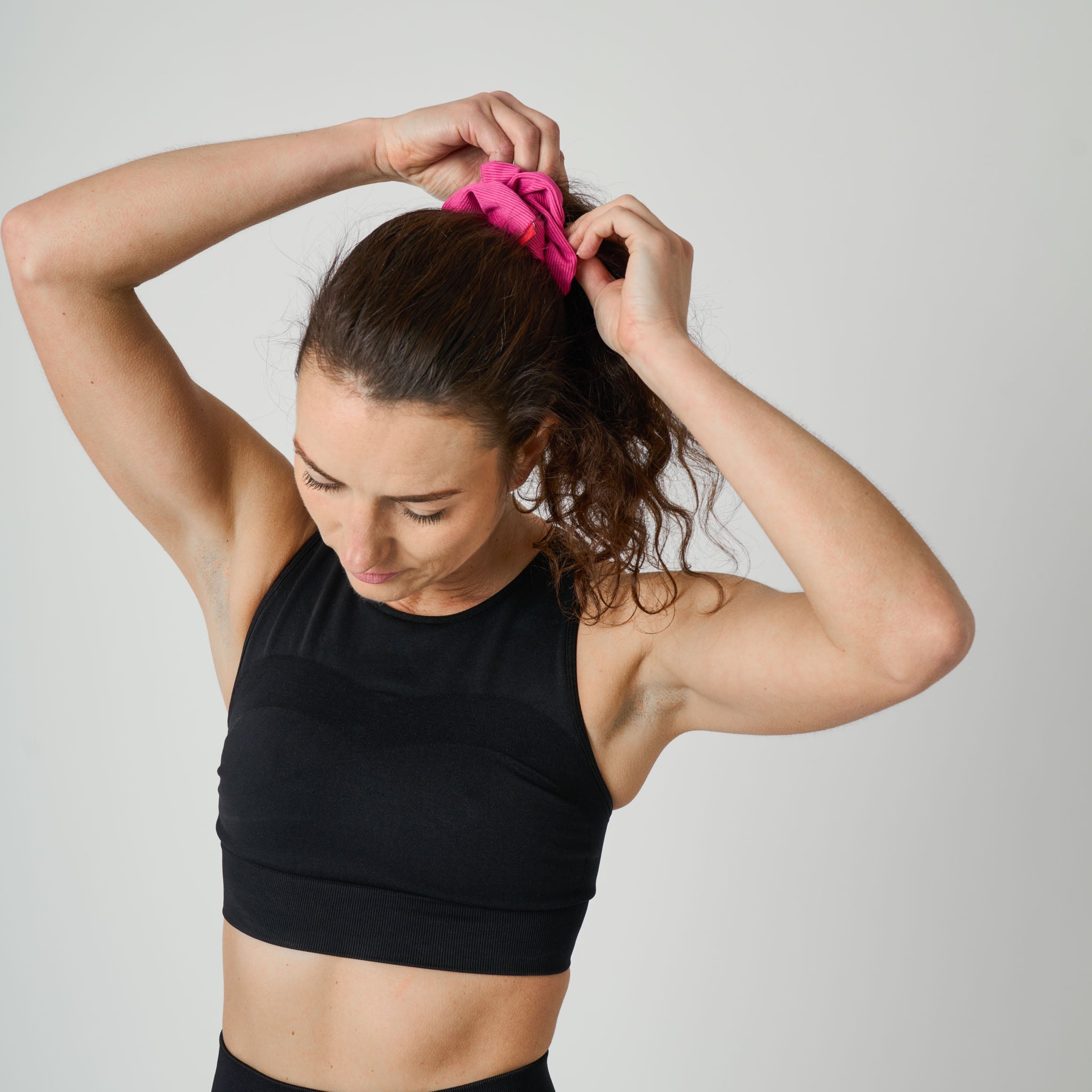 Woman tying a pink scrunchie in her hair against a plain background