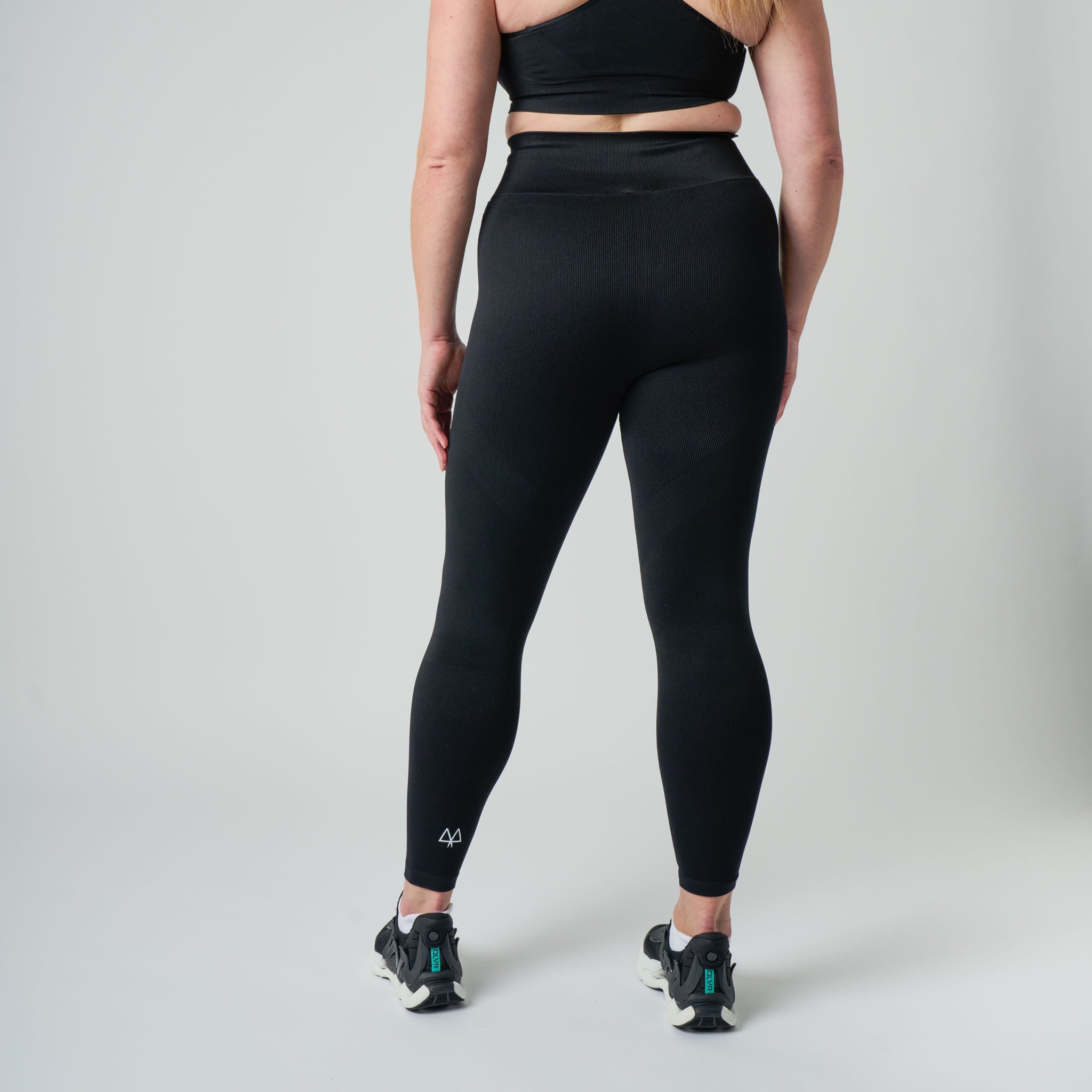 Person wearing black athletic leggings and top on a plain background