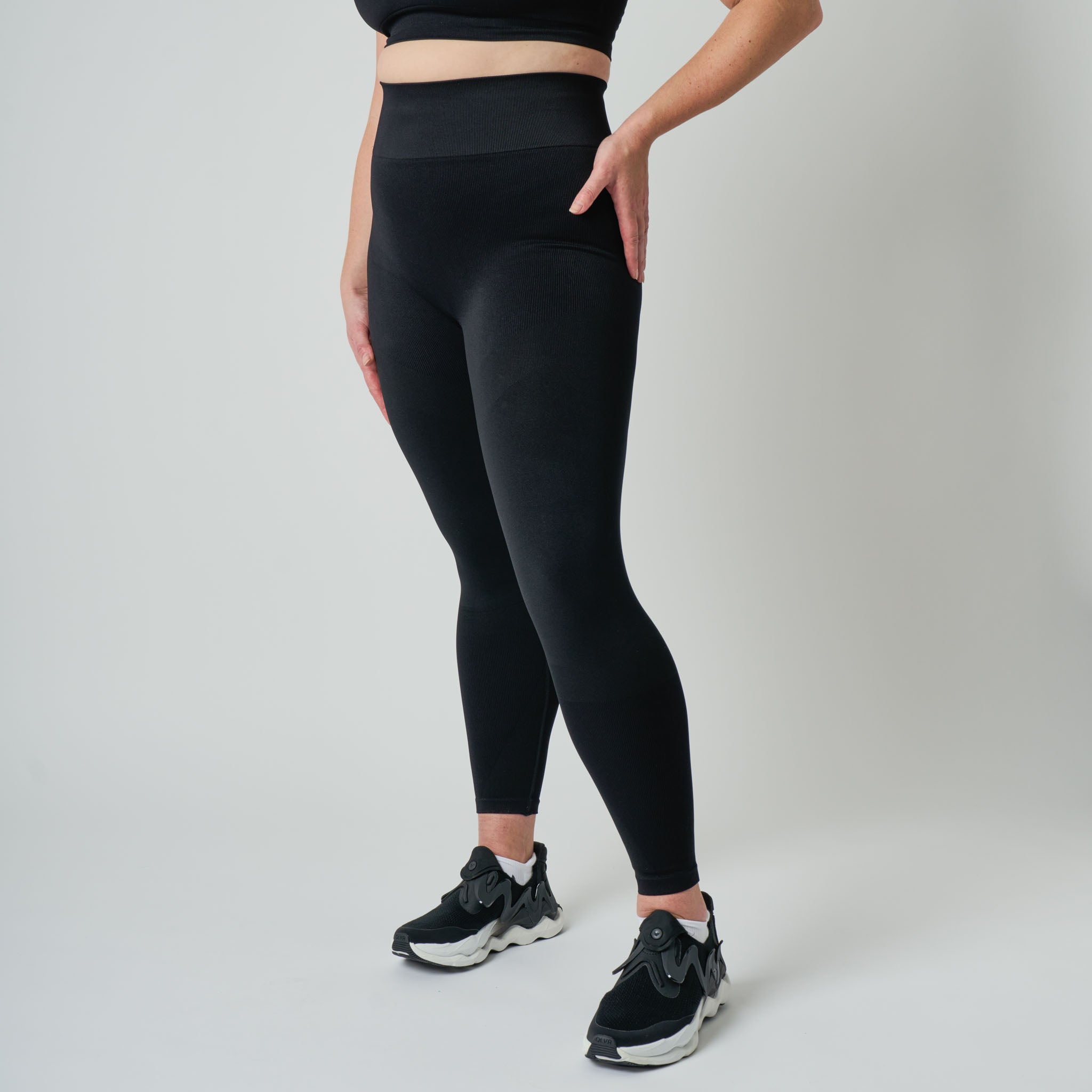 Person wearing black leggings and black sneakers on a light gray background