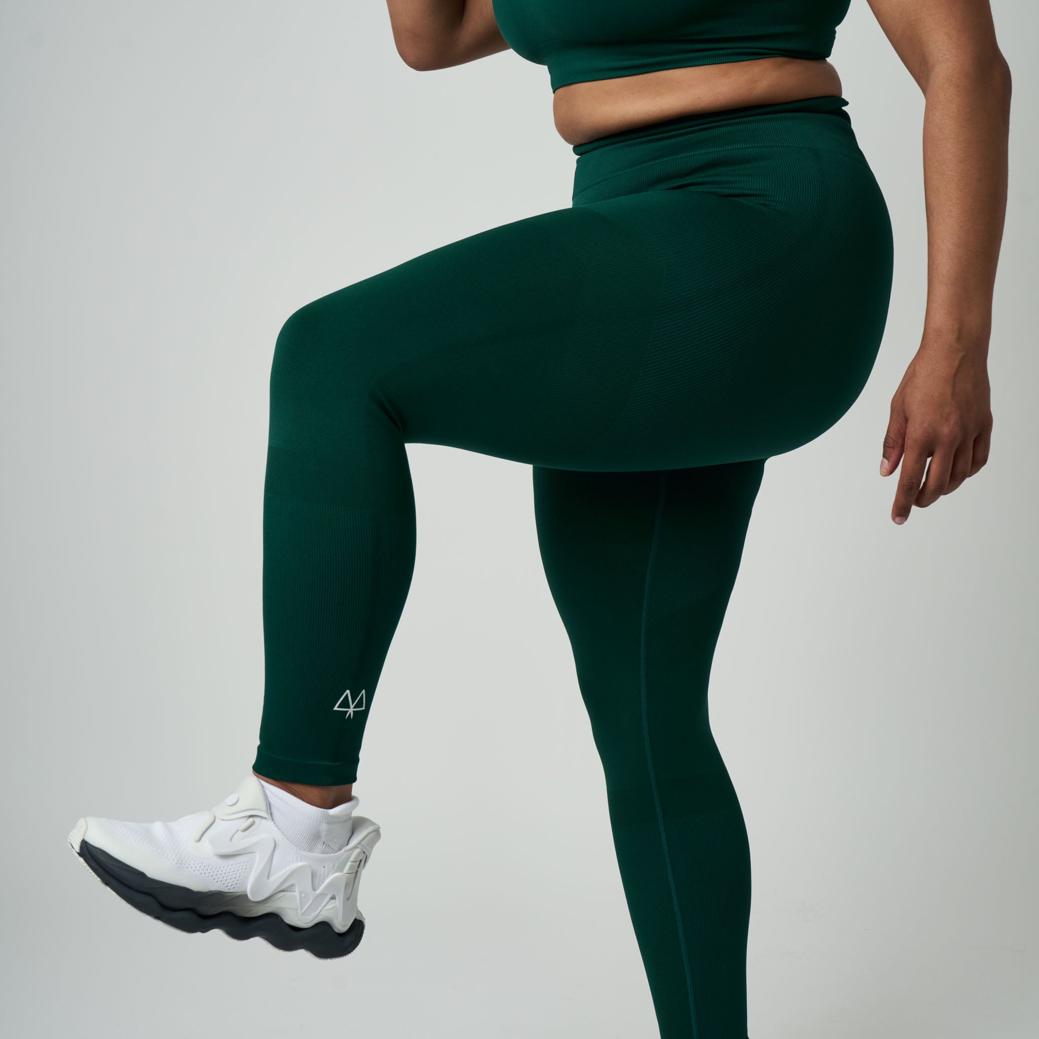 Person wearing green leggings and white sneakers on a light gray background