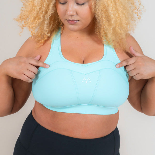 Woman wearing MAAREE Empower Sports Bra in Spearmint Green colour pointing at the Overband Technology