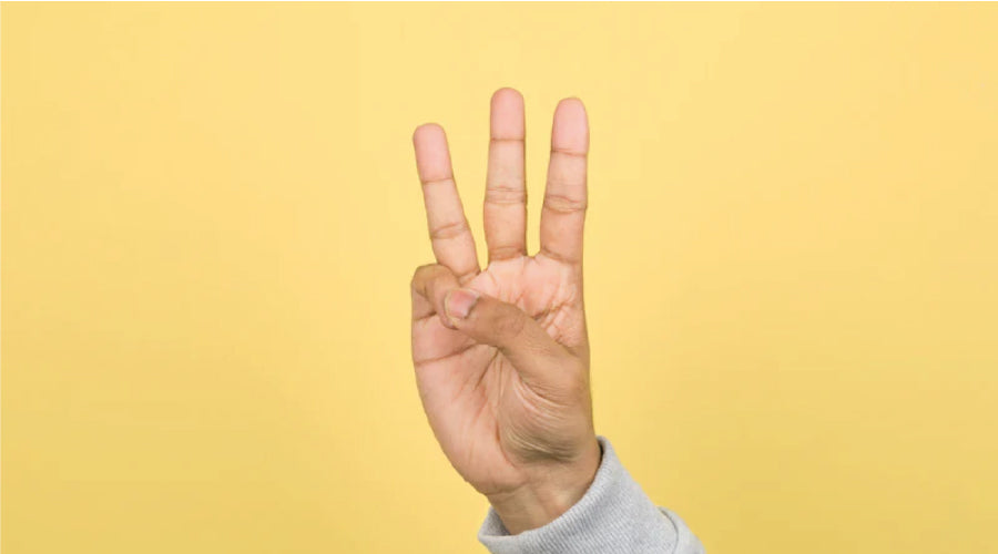Caucasian hand holding up three fingers on a yellow backdrop