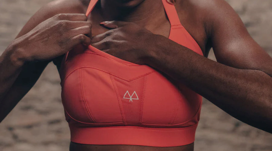 Black lady wearing a Coral coloured Maaree sports bra and adjusting herself