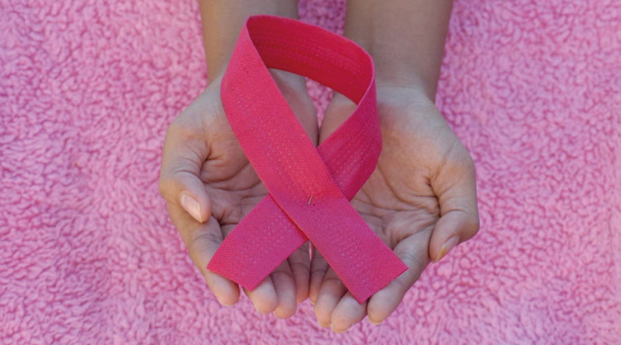 Pair of hands holding a pink breast cancer awareness ribbon against a fluffy pink floor