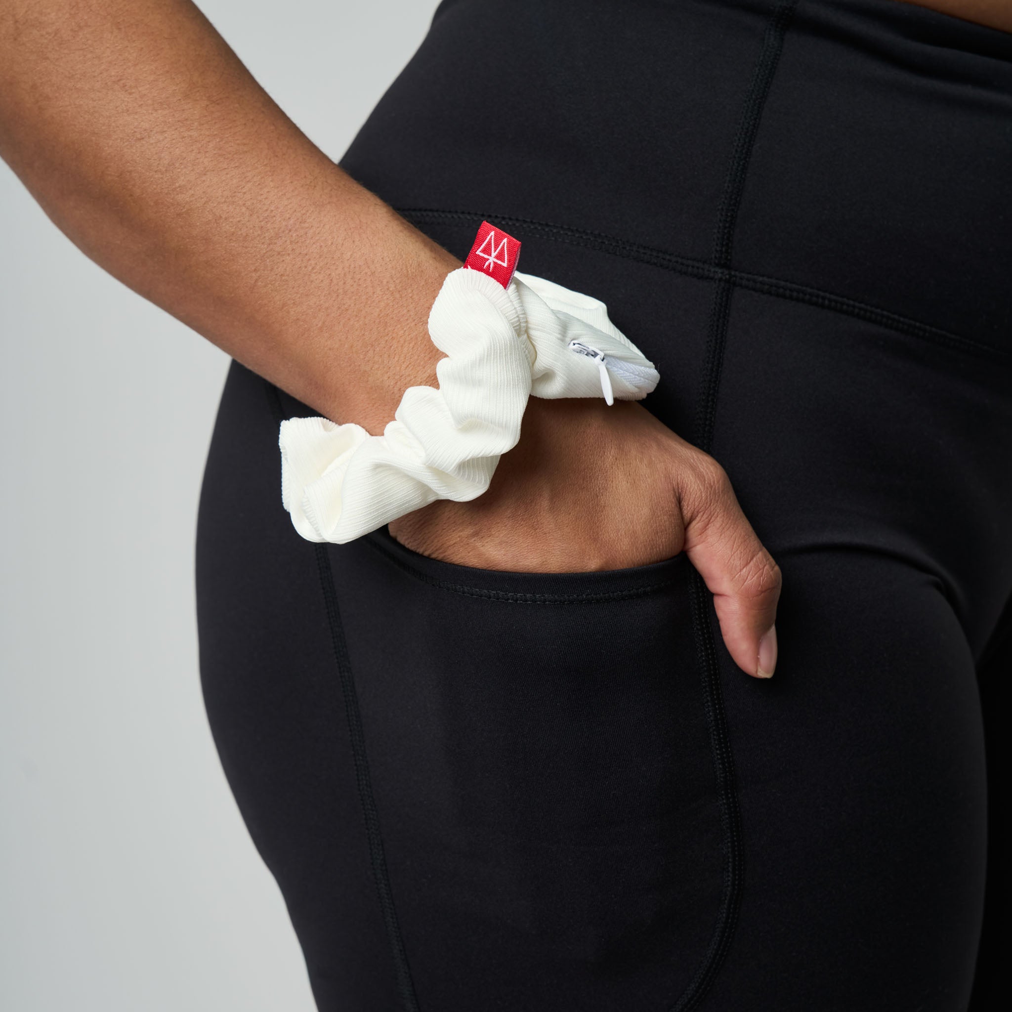Person wearing a white scrunchie with a red tag on a plain background