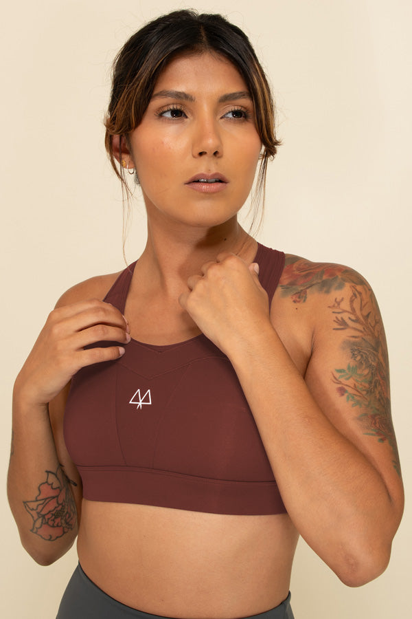 Woman in Burgundy high-support sports bra facing forward, showing the White MAAREE logo on the chest, playing with the straps of the bra.