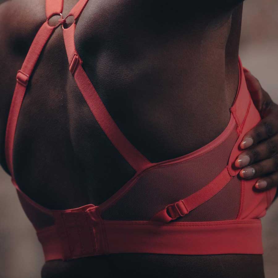 Athlete Abazz wearing the High Impact Sports Bra in Coral, adjusting the Overband at the side.