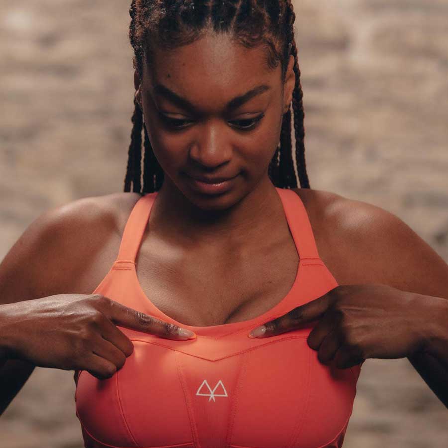 Runner Abazz pointing at the Overband on the MAAREE Solidarity high impact sports bra in coral.